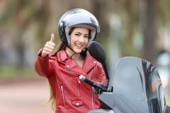 Motorcyclist giving a thumbs-up while seated on her bike outdoors by the roadside, seeking affordable motorcycle insurance - Cheap motorcycle insurance in CA