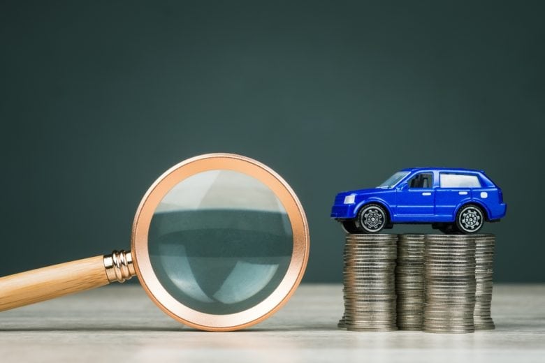 Blue toy car on top of a row of coins next to a magnifying glass - Cheap auto insurance in California