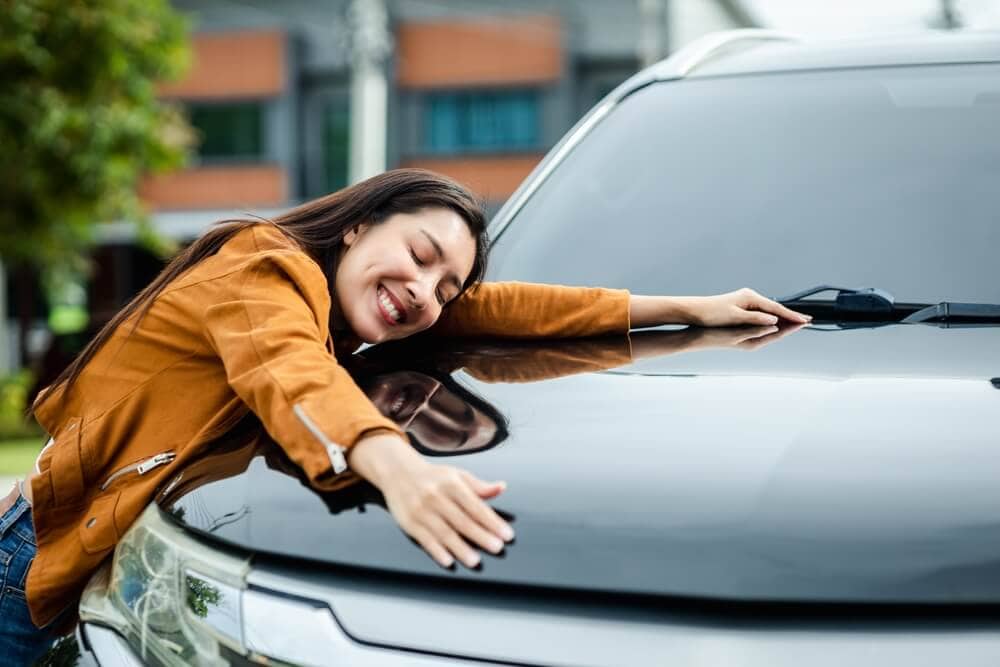 Woman smiling and hugging her vehicle, delighted to have the cheapest car insurance in California with the best savings from Cost-U-Less
