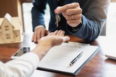 Real estate man in suit handing keys to new homeowner - Cheap homeowners insurance in California