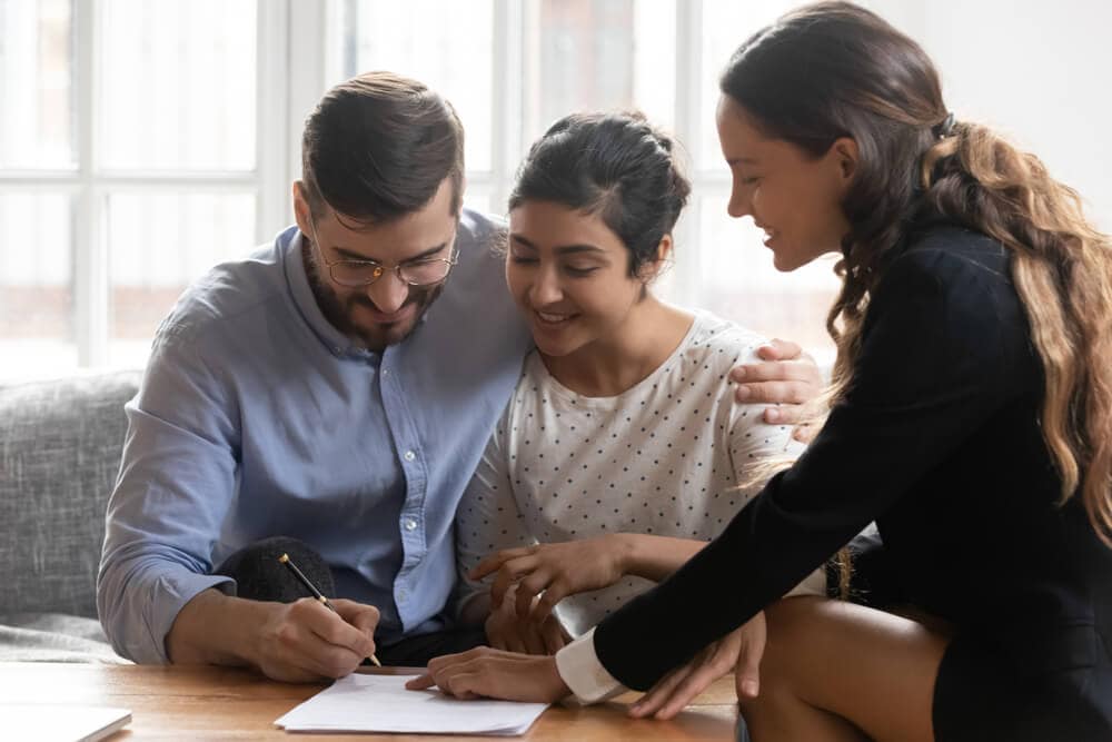 Young couple with real estate agent signing contract - Cheap homeowners insurance in California