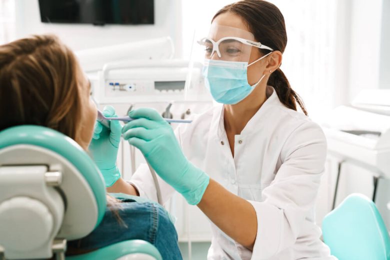 Woman sits in dental chair getting dental services from a female dentist.