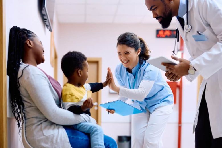 Child sitting on his mom's lap high fiving the female doctor.