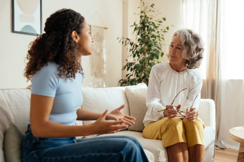 Young African American woman sitting on a couch talking to a mature Caucasian therapist.