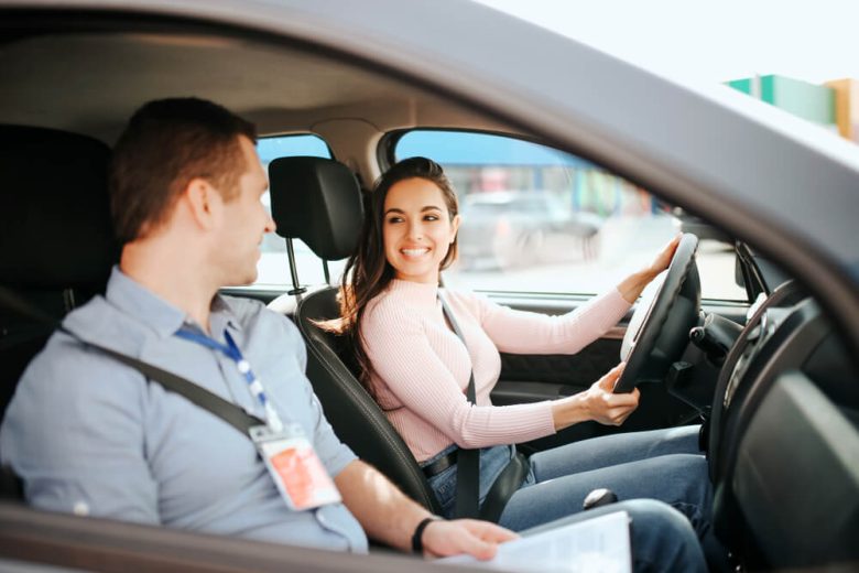 Young woman driver takes her driving test with the instructor sitting in the seat next to her - cheap car insurance in California.