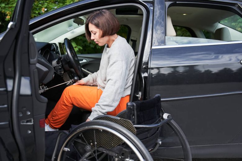 A woman exits the driver's seat and gets into her wheelchair parked next to the car.