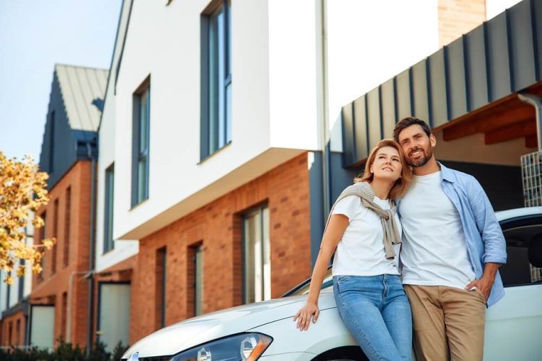 A couple leans against their car in front of their home - cheapest car insurance in California.