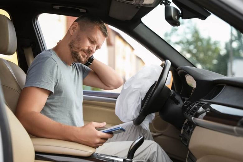 A man rubs his neck, sitting behind the wheel of his car after an accident where the airbag has deployed.