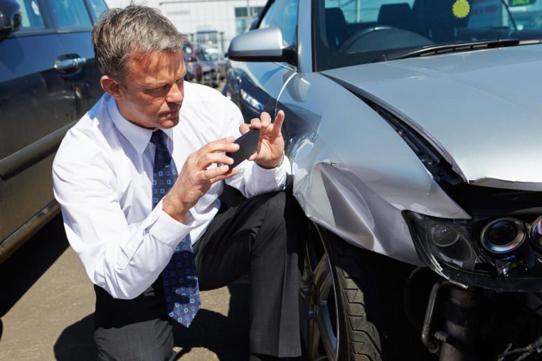 An insurance adjuster takes pictures of a car involved in a collision - cheap collision insurance in California.